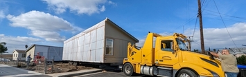 View of a large truck with part of a prefabricated home on the bed.