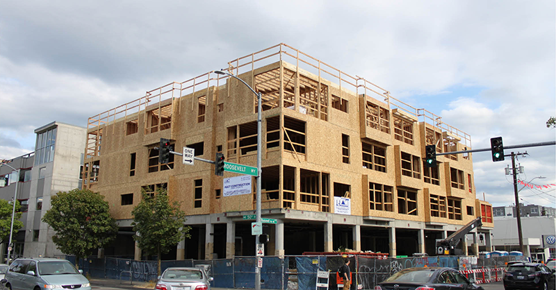 Photograph of a three-story wood apartment building being constructed about a concrete podium in Seattle.