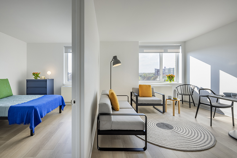 View of an apartment unit in 1490 Southern Boulevard, showing bedroom and living room with white-painted walls, woods floors, and sunlight streaming in.