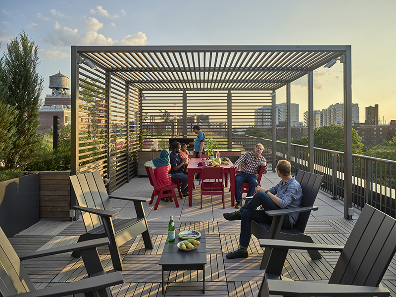 Roof deck of OneFlushing, with trellis, seating for residents, and view of NYC. Residents are grilling and sitting around talking.