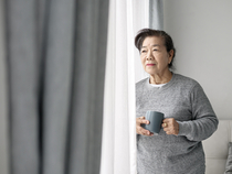 Older woman looking out window while holding mug.