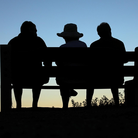 Three olders adults sitting on a bench at sunset.