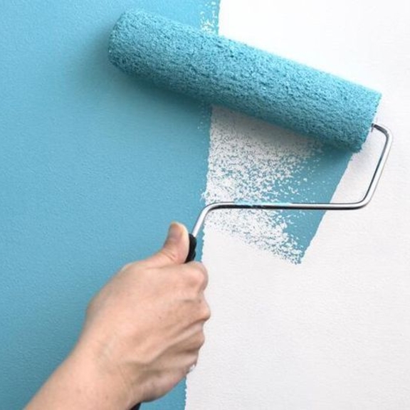 A hand rolling blue paint onto a wall.