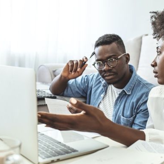 Black couple reading upsetting information on computer screen.