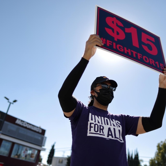 Masked person holding "Fight for $15" sign.