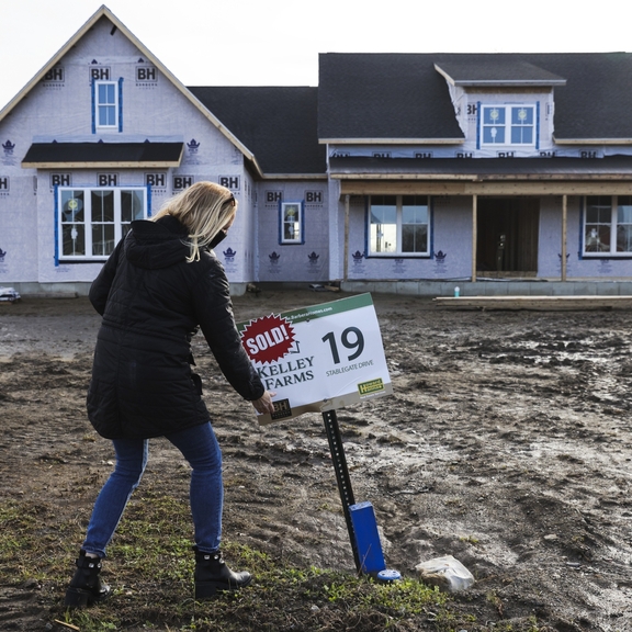 Woman planting "sold" sign in front of house under construction.