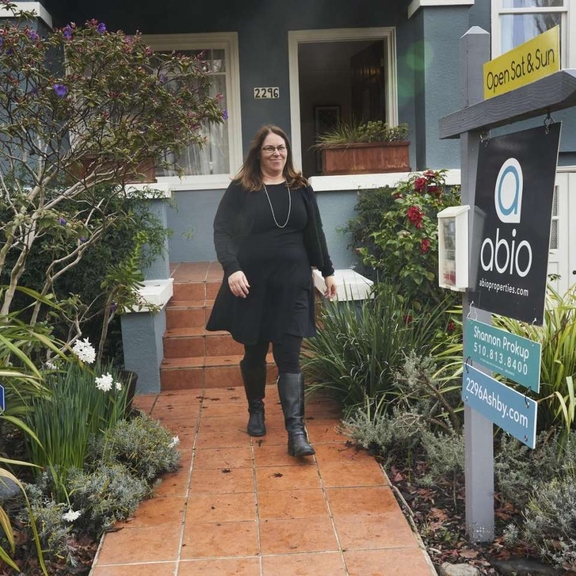 Woman standing in front of house with realtor sign.