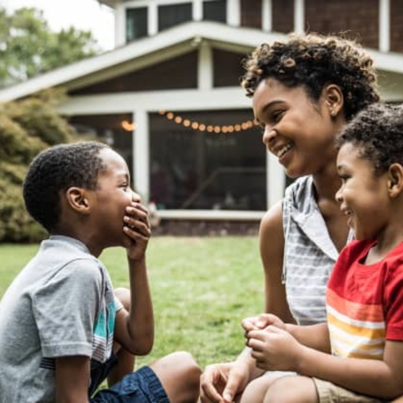 Woman laughing with two children in yard in front of large house.