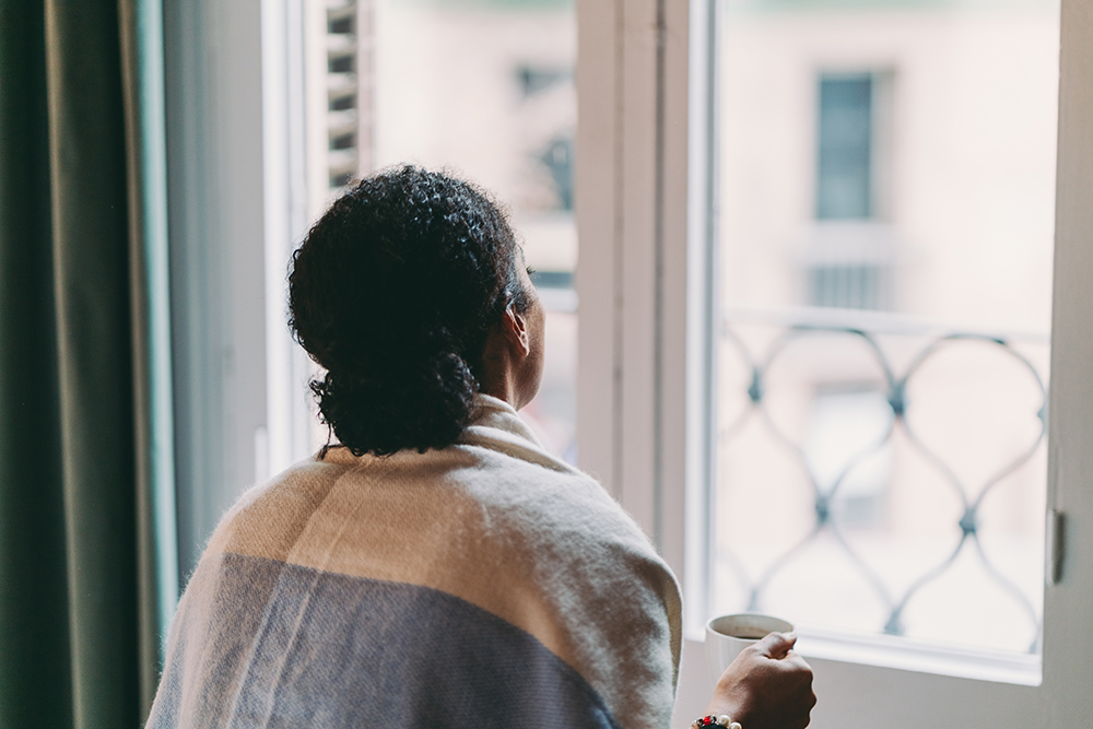 Woman wrapped in shawl staring out of a closed window.