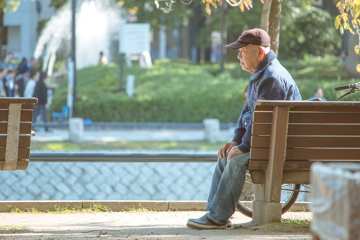 Older man sitting on bench outside.
